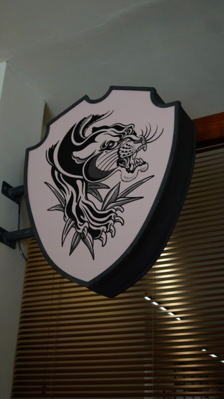 Banderola con forma de escudo colgada del techo, con una pantera negra rugiendo pintada en blanco y negro.
