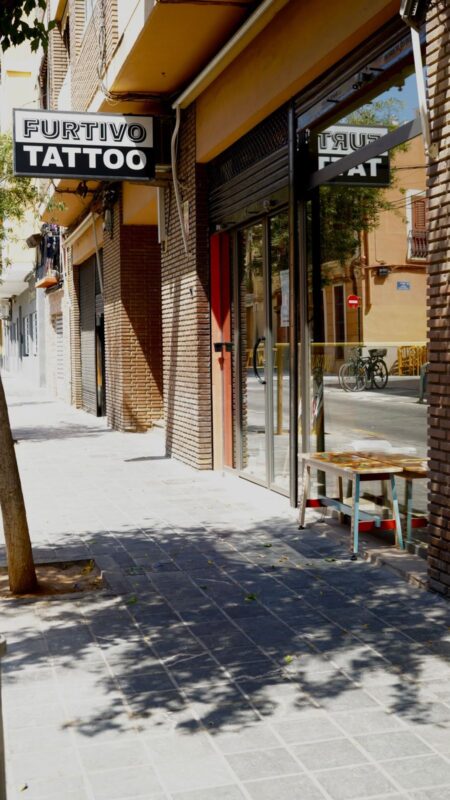 Fachada de Furtivo Tattoo en la acera, con la banderola blanca y negra que pone FURTIVO TATTOO.