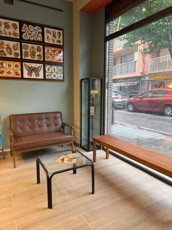 Sala de espera con sofá de piel marrón, mesa baja de cristal, vitrina y láminas de flash enmarcadas en la pared verde.