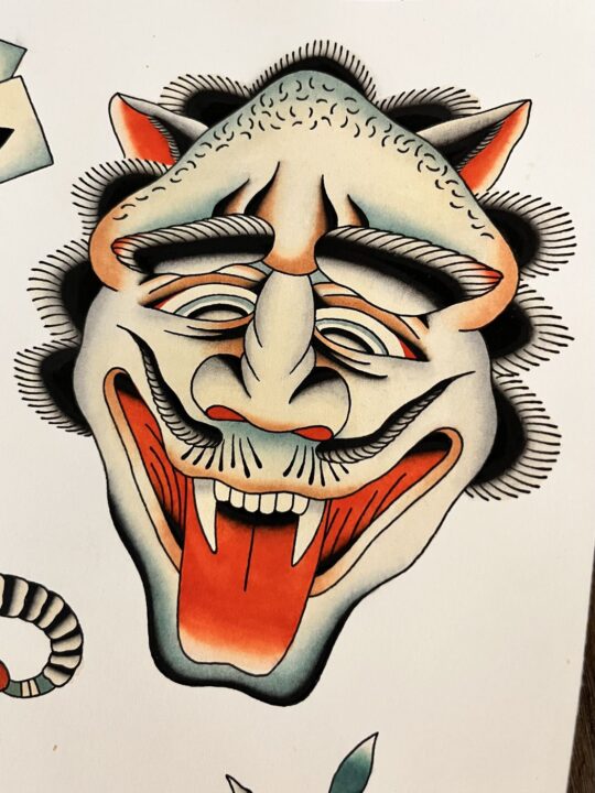 Lámina de flash pintada a mano: máscara de demonio con cuernos, colmillos y lengua roja fuera.
