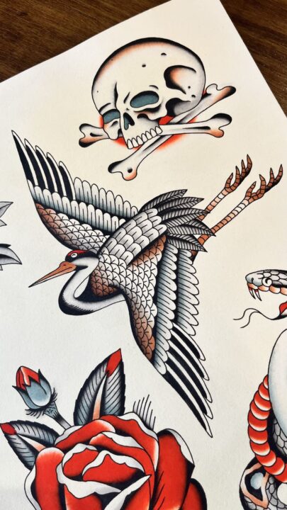 Lámina de flash pintada a mano: grulla en vuelo bajo una calavera con dos huesos cruzados y una rosa roja.