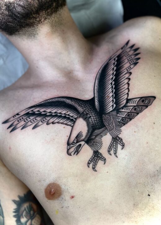 Águila con las alas abiertas y las garras por delante, tatuada en el pecho en negro y gris.