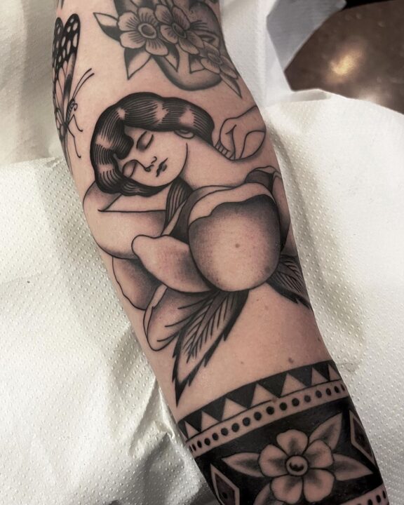 Mujer dormida abrazada a un melocotón, tatuada en el antebrazo en negro y gris.