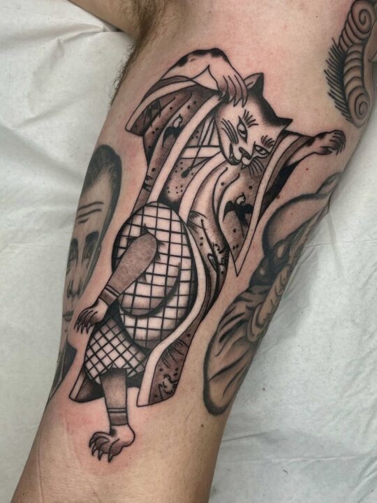 Gato vestido con kimono a rayas y prenda de rejilla, tatuado en la pierna en negro y gris.