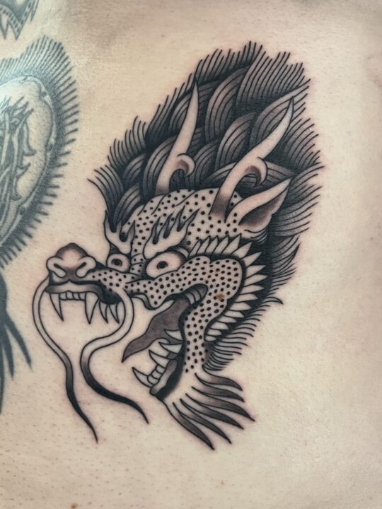 Cabeza de dragón japonés con melena y bigotes, tatuada en el costado en negro y gris.