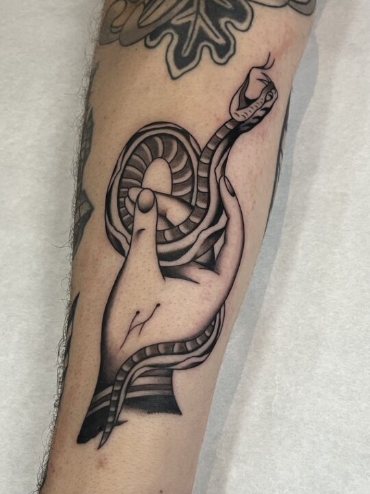 Mano abierta con una serpiente enroscada alrededor de los dedos, tatuada en el antebrazo.
