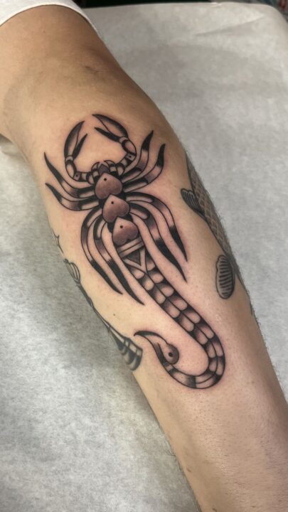 Escorpión con las patas extendidas y la cola curvada hacia abajo, tatuado en la pierna.