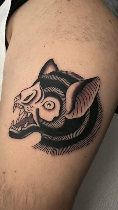 Cabeza de pantera con el rostro descarnado hasta el hueso, tatuada en el muslo en negro y gris.