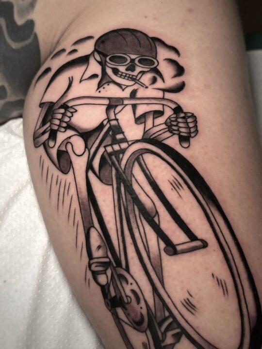 Esqueleto con casco y cigarrillo montado en una bicicleta de carreras, tatuado en el brazo.
