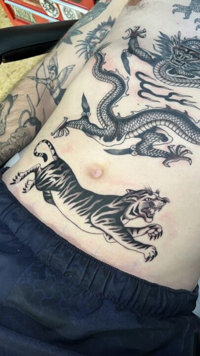Dragón japonés en el costado y un tigre saltando sobre el vientre, tatuados en negro y gris.