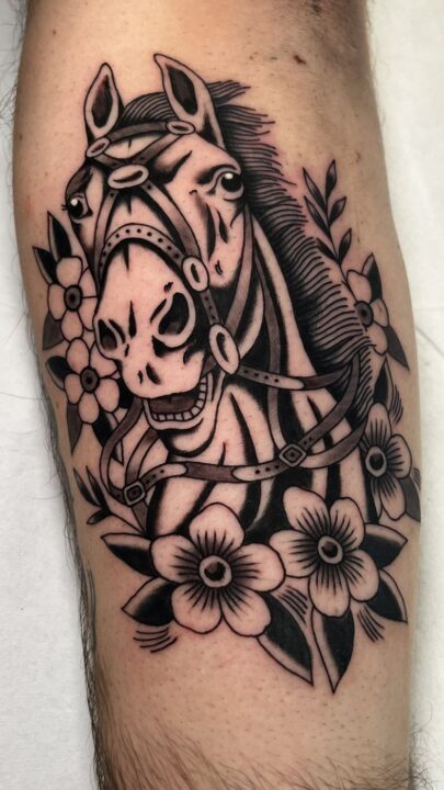 Cabeza de caballo con brida rodeada de flores de cinco pétalos, tatuada en la pierna.