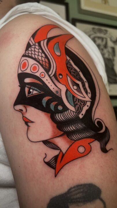 Perfil de mujer con un antifaz de formas curvas en rojo, negro y azul claro, tatuado en el hombro.