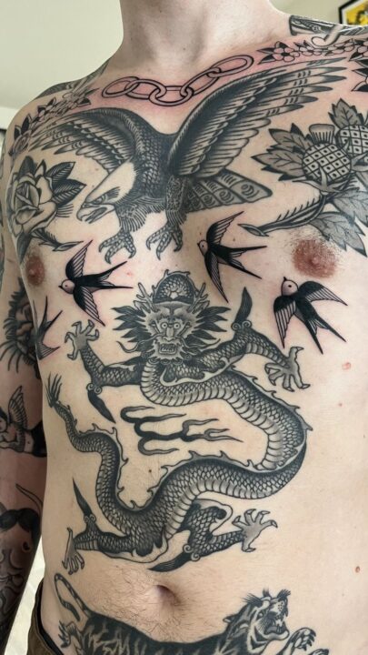 Detalle del torso tatuado: el águila del pecho, las golondrinas y el dragón del vientre en negro y gris.