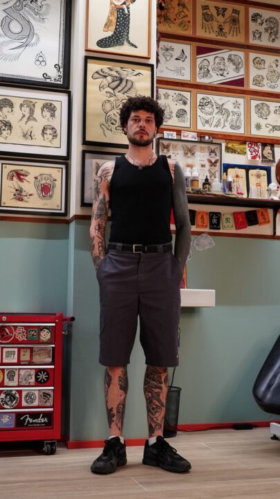 Augusto Cabrera de cuerpo entero en su cabina, con los brazos y las piernas tatuados, delante de la pared de flash.